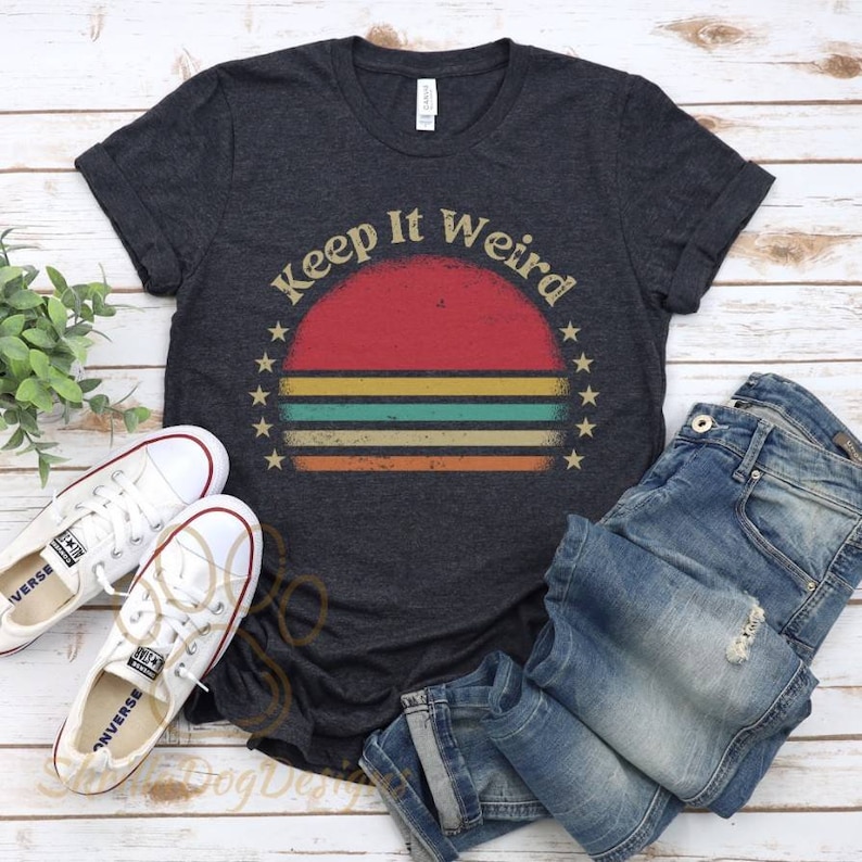 Puede incluir: Una camiseta gris oscuro con un gr&aacute;fico de puesta de sol de estilo vintage y el texto "Keep It Weird".