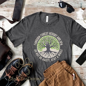 May include: A dark gray t-shirt with a circular design featuring a tree with green leaves and roots. The text "Fangorn Forest Resort and Spa" is written around the tree, and the text "Do not be hasty, stay a while" is written below the tree.