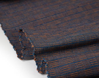 May include: Close-up of a woven fabric with a blue and brown striped pattern. The fabric has a textured surface and a slightly frayed edge.