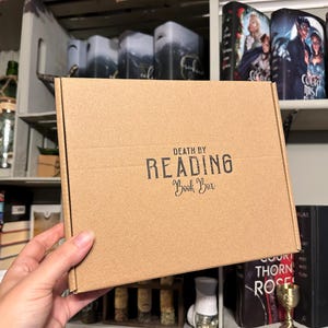 May include: A brown cardboard box with the text "DEATH BY READING Book Box" printed on the front.