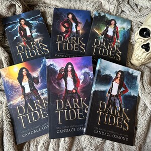 Peut inclure: Un ensemble de six livres brochés avec une couverture bleu foncé, violette et rouge représentant une femme en veste rouge et pantalon noir debout devant une mer orageuse. Les titres des livres sont "The Siren's Call", "The Gilded Stone", "The Dark Tides", et "The Forsaken", tous en lettres dorées. Les livres sont de l'auteure à succès du USA Today Candace Osmond.