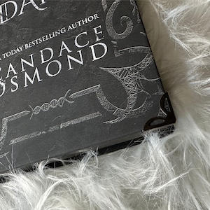 May include: Close-up of a black book with a silver embossed design and the text "USA TODAY BESTSELLING AUTHOR CANDACE OSMOND".