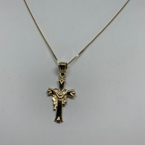 May include: A gold chain necklace with a gold cross pendant. The cross has a detailed design with a draped fabric.