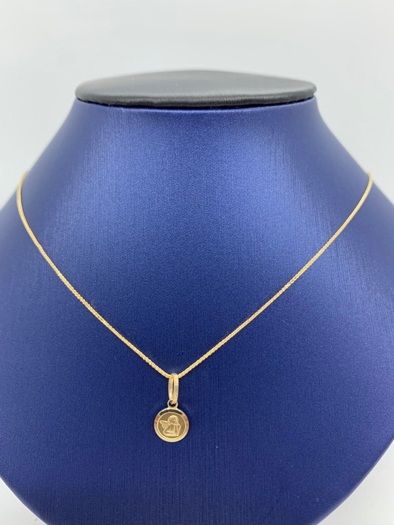 Op de afbeelding: Een gouden ketting met een klein rond hanger met een engelontwerp.