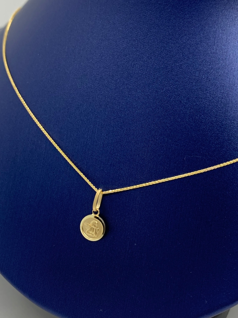 Op de afbeelding: Een gouden ketting met een klein rond hanger met een engelontwerp.