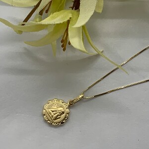 Puede incluir: Un collar de cadena de oro con un peque&ntilde;o colgante redondo con un dise&ntilde;o de &aacute;ngel.