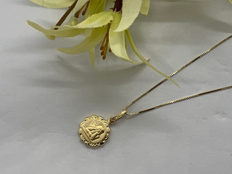 Puede incluir: Un collar de cadena de oro con un peque&ntilde;o colgante redondo con un dise&ntilde;o de &aacute;ngel.