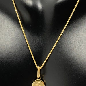 Op de afbeelding: Een gouden ketting met een klein rond hanger met een engelontwerp.