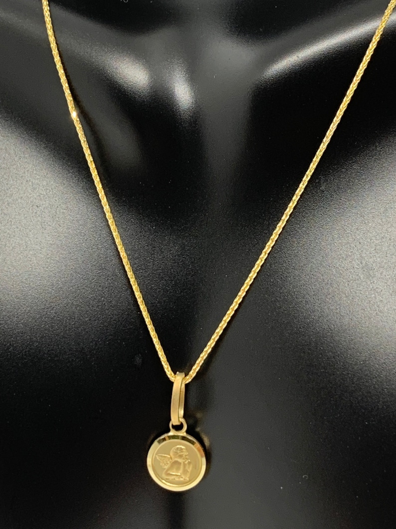 Op de afbeelding: Een gouden ketting met een klein rond hanger met een engelontwerp.