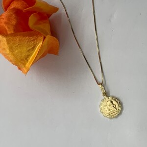 Puede incluir: Un collar de cadena de oro con un peque&ntilde;o colgante redondo con un dise&ntilde;o de &aacute;ngel.