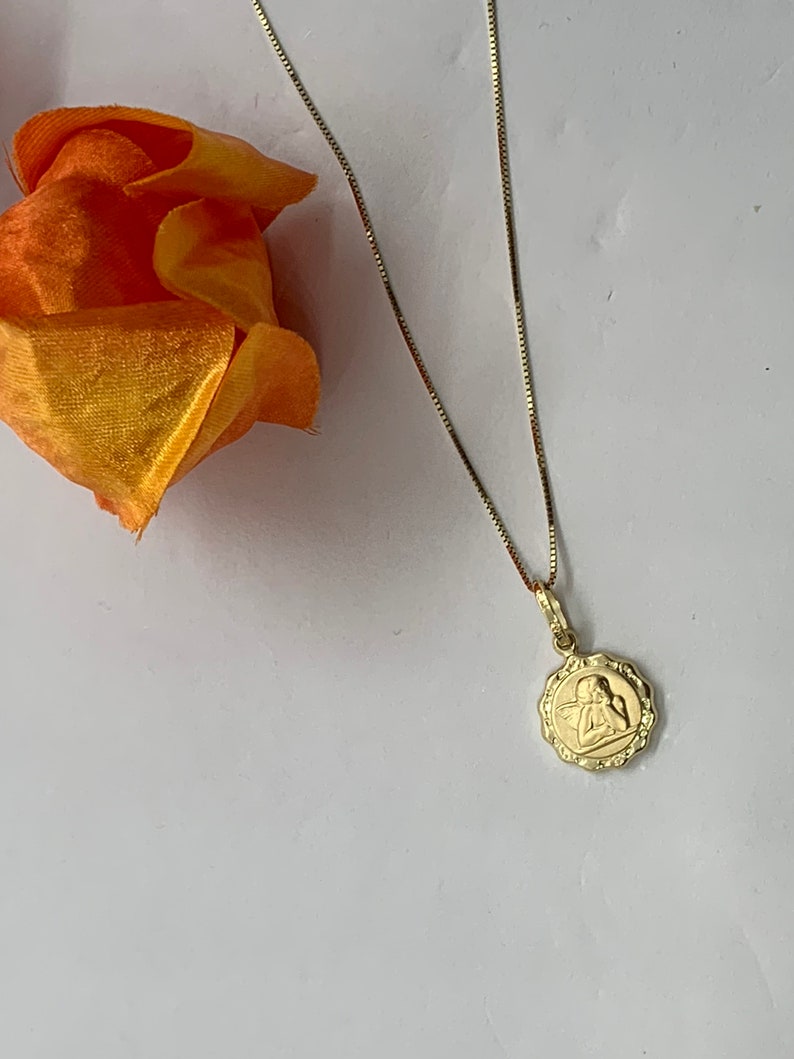 Puede incluir: Un collar de cadena de oro con un peque&ntilde;o colgante redondo con un dise&ntilde;o de &aacute;ngel.