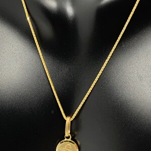Op de afbeelding: Een gouden ketting met een klein rond hanger met een engelontwerp.
