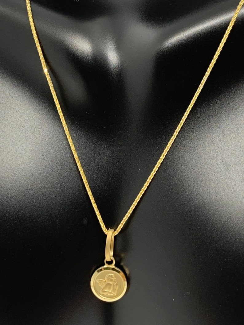 Op de afbeelding: Een gouden ketting met een klein rond hanger met een engelontwerp.
