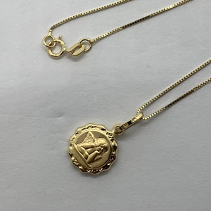 Puede incluir: Un collar de cadena de oro con un colgante redondo que presenta una imagen detallada de un &aacute;ngel con alas.