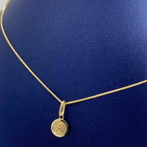 Op de afbeelding: Een gouden ketting met een klein rond hanger met een engelontwerp.