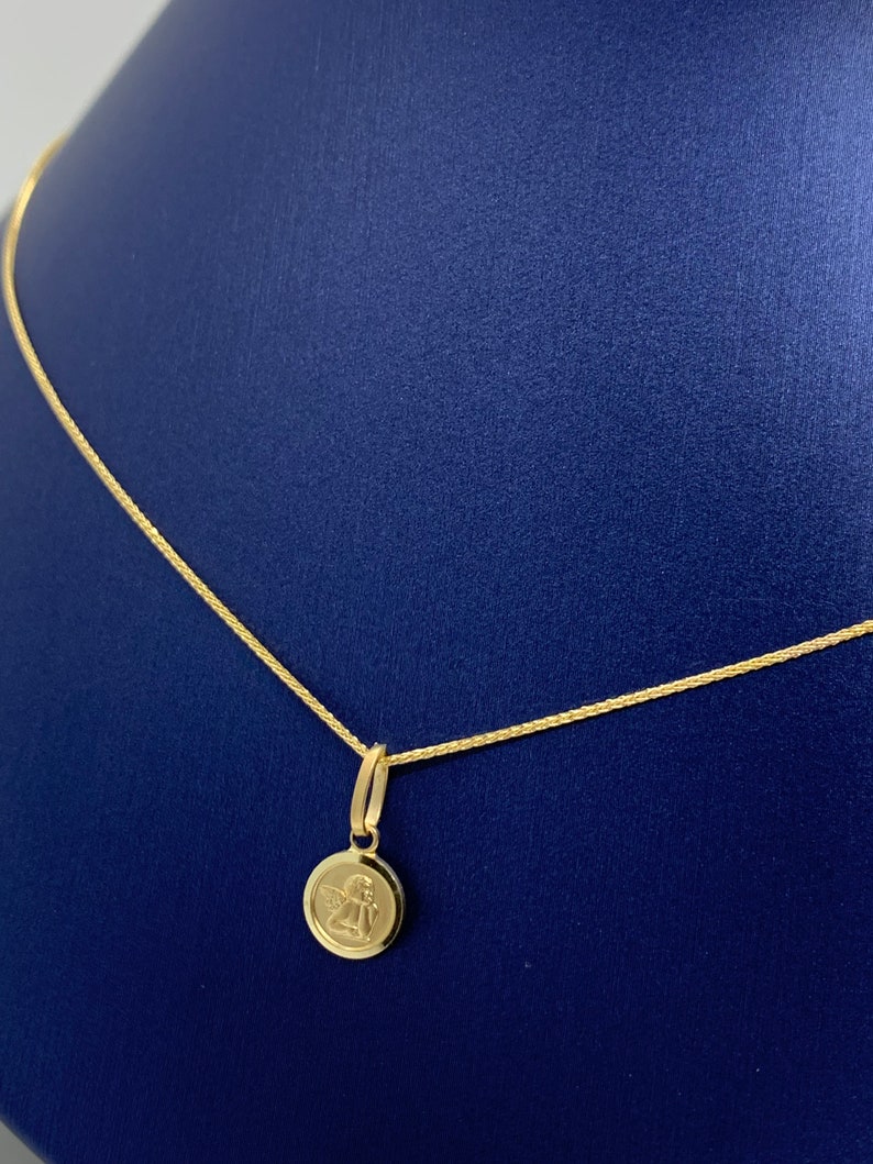 Op de afbeelding: Een gouden ketting met een klein rond hanger met een engelontwerp.