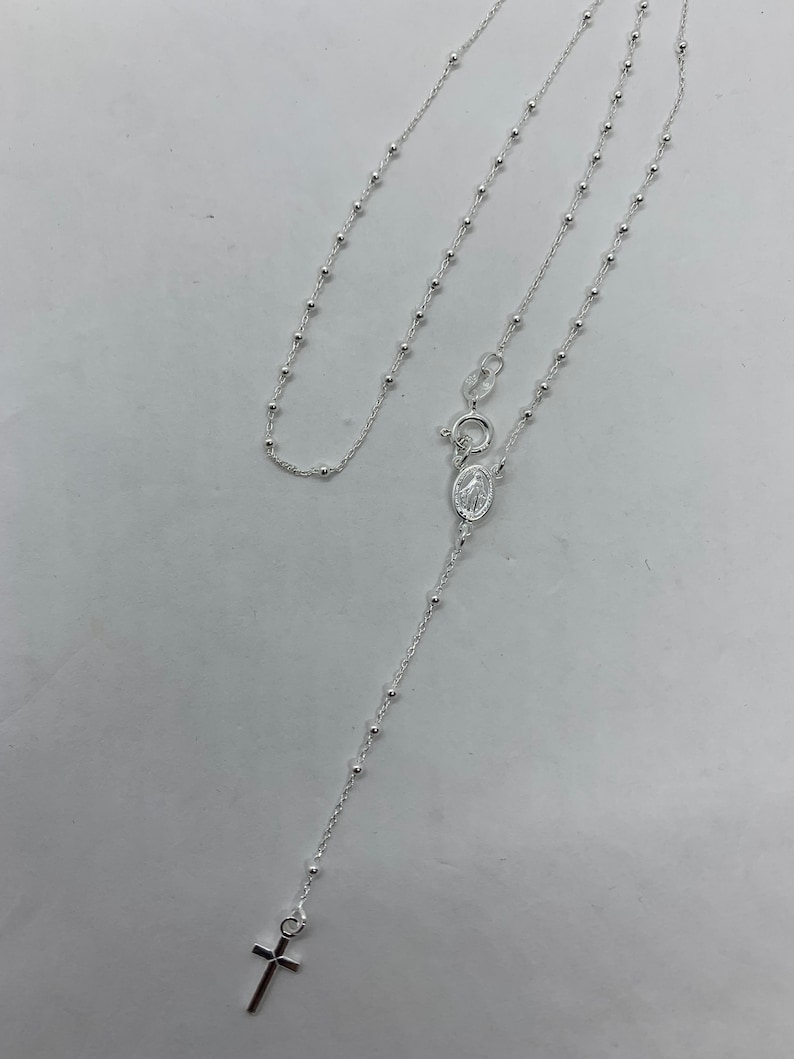 May include: A silver rosary necklace with a small cross charm and a silver oval pendant with a religious image.