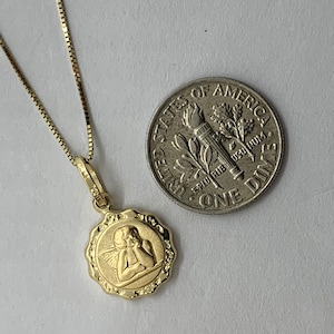 Puede incluir: Collar de cadena de oro con un peque&ntilde;o colgante redondo con un dise&ntilde;o de querub&iacute;n. El colgante es del tama&ntilde;o de una moneda de diez centavos.