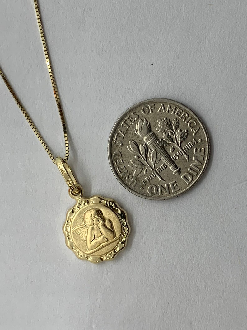 Puede incluir: Collar de cadena de oro con un peque&ntilde;o colgante redondo con un dise&ntilde;o de querub&iacute;n. El colgante es del tama&ntilde;o de una moneda de diez centavos.