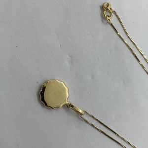 Puede incluir: Un collar de cadena de oro con un colgante redondo y festoneado.