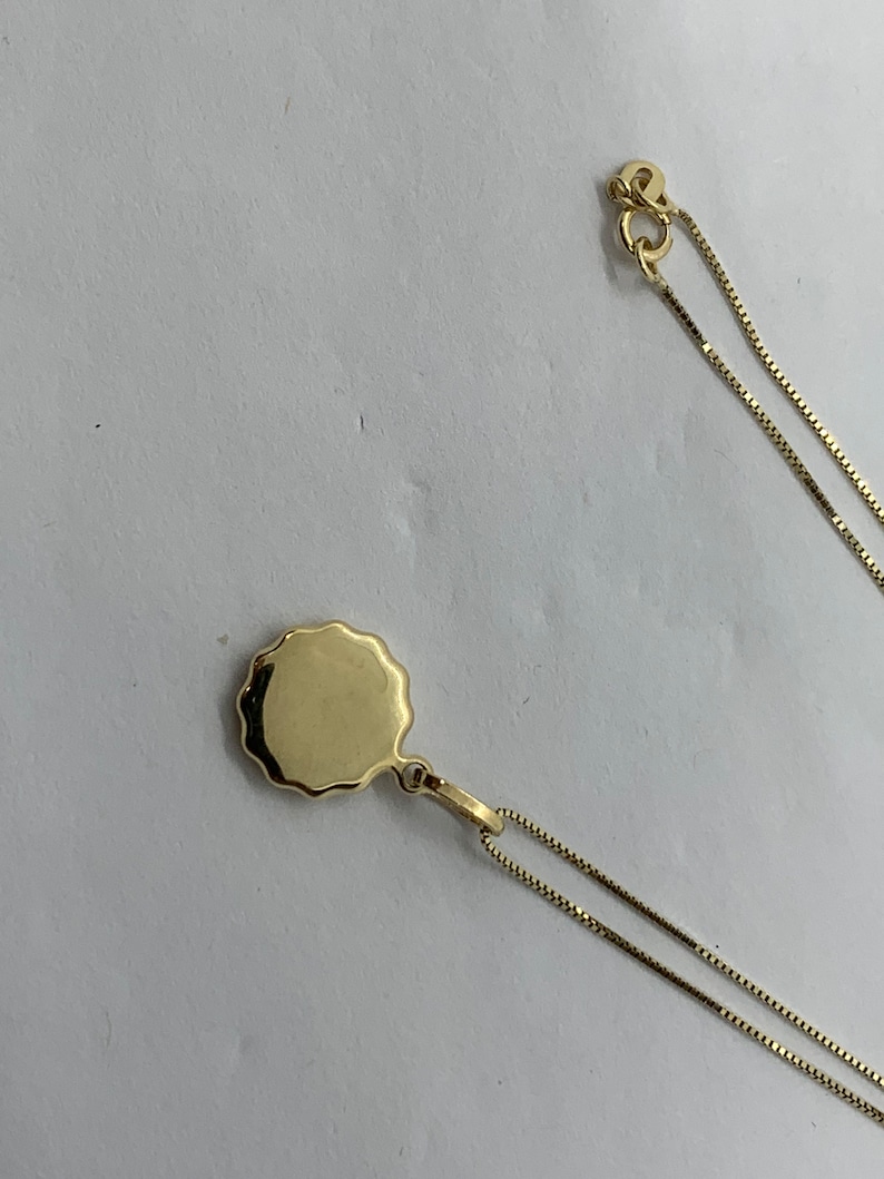 Puede incluir: Un collar de cadena de oro con un colgante redondo y festoneado.