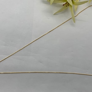 Op de afbeelding: Een gouden ketting met een klein rond hangertje.