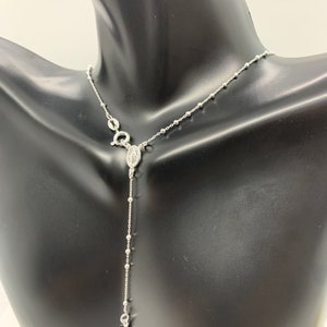 May include: A silver rosary necklace with a small cross charm and a pendant featuring the Virgin Mary.