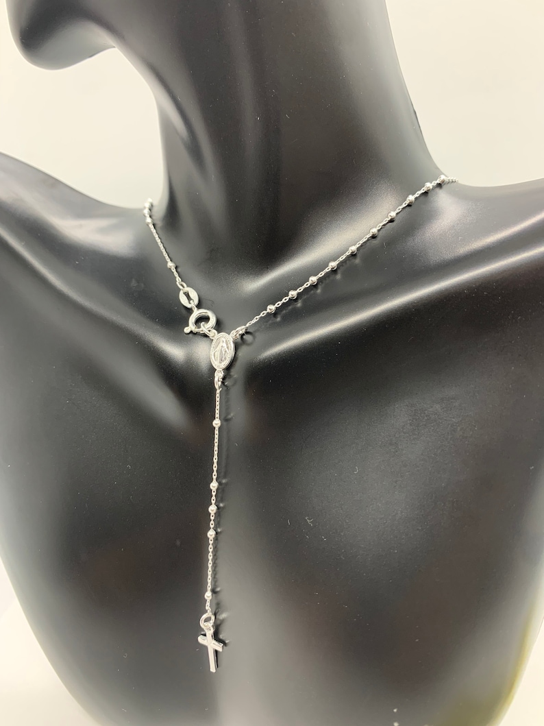 May include: A silver rosary necklace with a small cross charm and a pendant featuring the Virgin Mary.