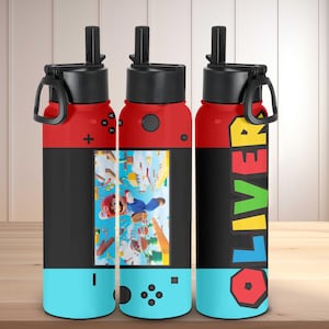 May include: A set of three water bottles with a video game theme. The top and handle are red, the middle section is black, and the bottom is light blue. One bottle features a video game scene, and another has the name "OLIVER" in colorful letters.