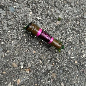 Puede incluir: Un producto enrollado marr&oacute;n con una banda rosa que dice "STIIIZY" en letras blancas. El producto descansa sobre una superficie gris texturizada. El extremo del producto es negro.