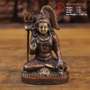May include: A bronze statue of Shiva, a Hindu deity, sitting in a meditative pose. He is holding a trident in his right hand and has a third eye on his forehead. The statue is 7 inches tall, 4 inches long, and 2 inches wide. It weighs 1.080 kg.