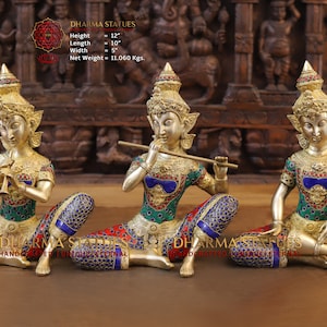 Puede incluir: Tres estatuas doradas de figuras tocando instrumentos musicales. Las figuras están sentadas con las piernas cruzadas y adornadas con joyas de colores. Las estatuas miden 30,48 cm de alto, 25,4 cm de largo y 12,7 cm de ancho. Pesan 5,02 kg.