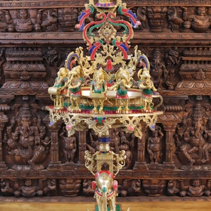 May include: A large, ornate, gold-coloured metal stand with a round top and three legs. The stand is decorated with colourful gemstones and features a small elephant figurine at the base. The stand is 51 inches tall, 21 inches long, and 18.5 inches wide. It weighs 45 kilograms.