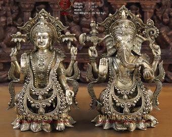 May include: Two ornate silver-colored statues of Hindu deities. The statue on the left is of Lakshmi, the goddess of wealth and prosperity, with four arms. The statue on the right is of Ganesha, the elephant-headed god of beginnings, success, and good fortune. Both statues are seated on lotus bases and are intricately detailed.