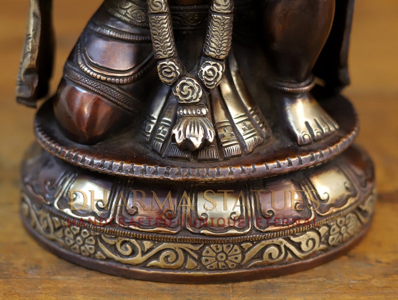 May include: A bronze statue of a deity with intricate details, including a beaded necklace and a patterned skirt. The statue is sitting on a round base with a silver-colored band and ornate carvings.