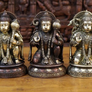 May include: Three gold and copper colored statues of the Hindu deity Hanuman, each with a different colored base. The statues are all in a kneeling position with their hands in a prayer position.
