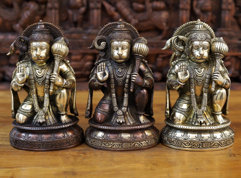 May include: Three gold and copper colored statues of the Hindu deity Hanuman, each with a different colored base. The statues are all in a kneeling position with their hands in a prayer position.