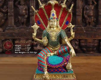 May include: A gold-colored statue of a Hindu deity sitting on a throne with a five-headed cobra hood. The statue is decorated with red, green, and blue gemstones. The statue is 17 inches tall, 8.5 inches long, and 8 inches wide. It weighs 11.7 kilograms. The text "DHARMA STATUES HANDCRAFTED UNIQUE ETERNAL" is on the base of the statue.