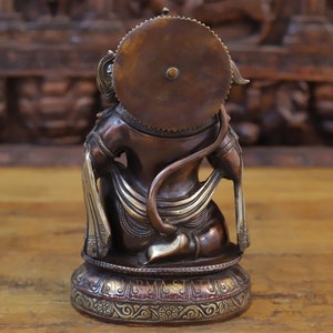 May include: A bronze statue of the Hindu deity Hanuman, sitting with his tail curled around his waist. He is wearing a crown and a decorative sash. The statue is on a base with intricate carvings.