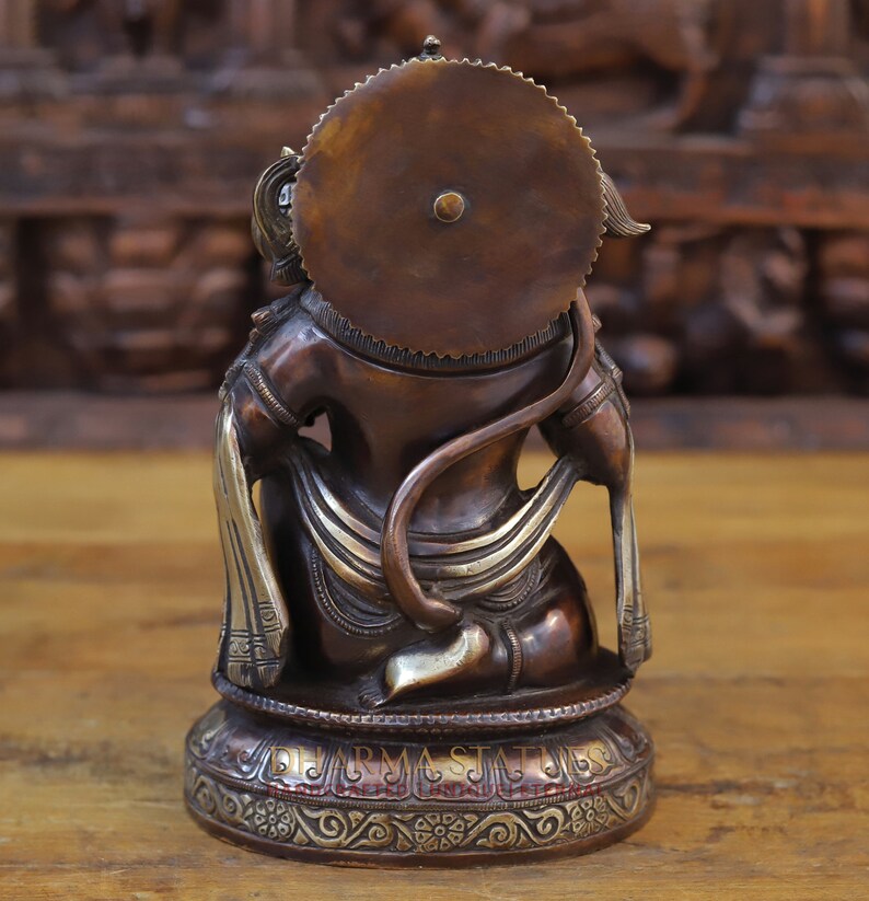 May include: A bronze statue of the Hindu deity Hanuman, sitting with his tail curled around his waist. He is wearing a crown and a decorative sash. The statue is on a base with intricate carvings.