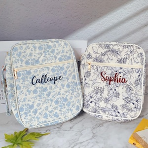 May include: Two floral-patterned bags with zippered closures. One bag features a light blue floral design with the name "Calliope" embroidered in navy. The other bag has a white background with a dark blue floral pattern and the name "Sophia" embroidered in red.