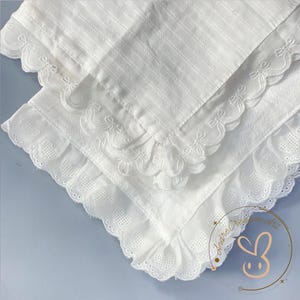 Puede incluir: Un cuadrado de tela blanca con un patr&oacute;n de rejilla texturizado y un borde decorativo. El borde est&aacute; rematado con un adorno de volantes decorado con formas de coraz&oacute;n bordadas y bordes festoneados, creando un aspecto detallado.