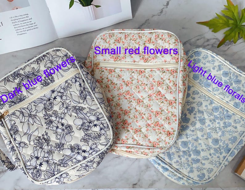 May include: Three quilted bags with floral patterns. One bag features dark blue flowers, another has small red flowers, and the third displays light blue florals. Each bag has a cream-colored zipper and a matching strap.