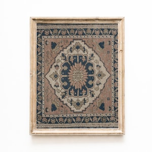 以下が含まれることがあります： 複雑で対称的なデザインの、額装された長方形のラグ。ラグは、中央にネイビーブルーのメダリオンと、同じ色の周囲のボーダーが特徴です。背景はくすんだローズ色で、クリーム色とオリーブグリーンのアクセントがあります。フレームは明るい木材です。