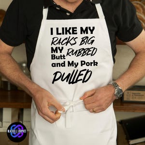 May include: White apron with the text "I LIKE MY RACKS BIG MY RUBBED Butt and My Pork PULLED" in black. The apron is being tied by a person. The Blackville Graphics logo is in the bottom left corner.