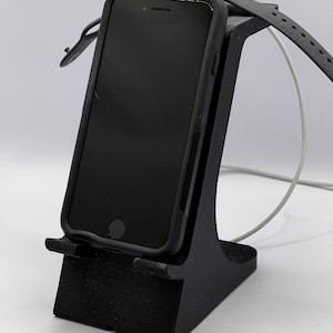 May include: A black 3D printed phone and smartwatch stand with a white charging cable.