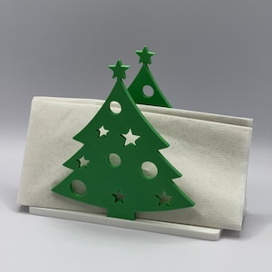 May include: Green Christmas tree-shaped napkin holder with cut-out stars and circles. The holder is made of wood and has a white base.