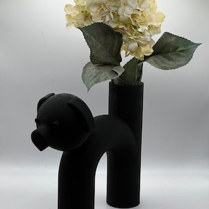 May include: Black ceramic vase shaped like a pig with a bouquet of white hydrangeas.