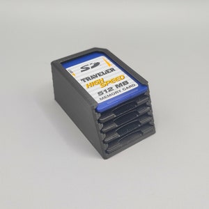 Könnte beinhalten: Schwarzer Kunststoff-Aufbewahrungskasten für SD-Speicherkarten. Der Kasten fasst mehrere Karten und trägt ein Etikett mit der Aufschrift "Traveler High Speed 512 MB Memory Card".