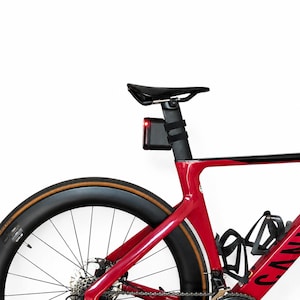 Könnte beinhalten: Ein rotes Rennrad mit schwarzem Sattel und Rücklicht an der Sattelstütze. Das Fahrrad hat einen schwarzen Reifen und einen Flaschenhalter. Das Fahrrad steht vor einem weißen Hintergrund.